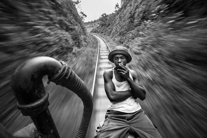 Un mécanicien du train de la FCE fume une cigarette à l'avant de la locomotive. Madagascar